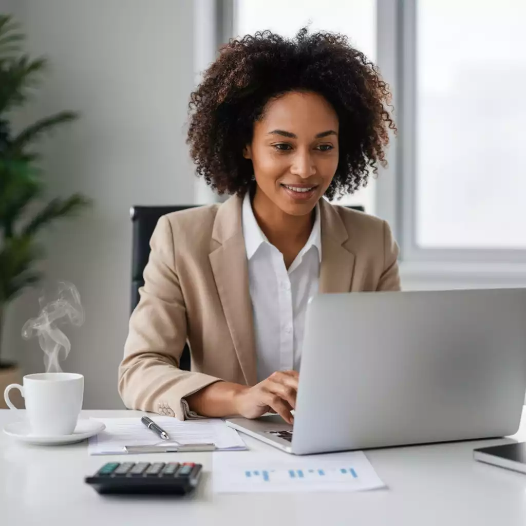 Person using a laptop to analyze mortgage documents, with a calculator and coffee on the table, bright and professional setting