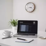 Laptop displaying calculator app on desk with notepad, pen, plant, and coffee cup; wall clock in background.