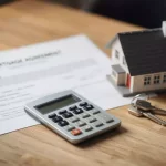 Calculator, keys, and model house on a mortgage agreement document, symbolizing real estate and financial planning.